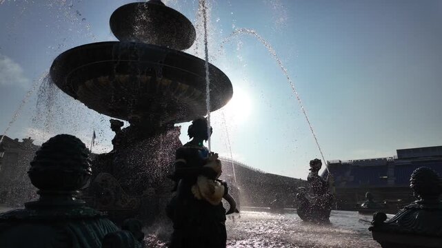 Fontaine des mers in place de la concorde, paris, france with water jets spraying high against a clear blue sky and bright sun, surrounded by allegorical sculptures and historic architecture