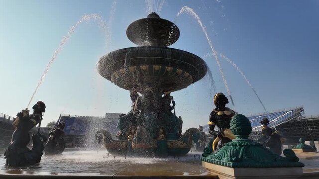 Fontaine des mers in place de la concorde, paris, france with water jets spraying high against a clear blue sky and bright sun, surrounded by allegorical sculptures and historic architecture