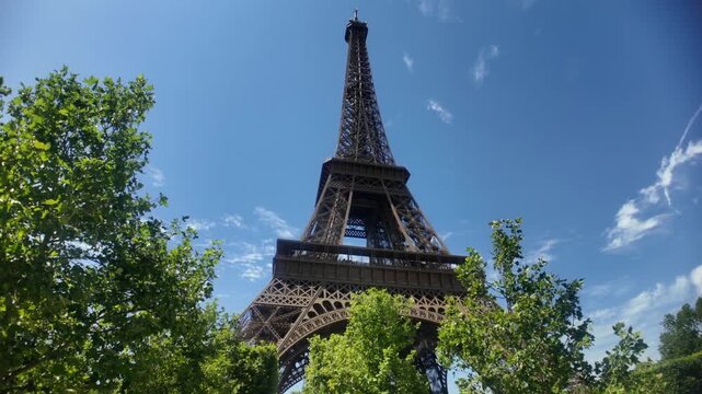 Majestic low-angle view of the eiffel tower in paris, france. The iconic landmark stands against a brilliant blue sky, beautifully framed by the lush green leaves of nearby trees