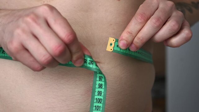 Excess weight.
The problem of obesity.
A man measures his waist with a measuring tape.
A man on a diet.
A man with a big belly.