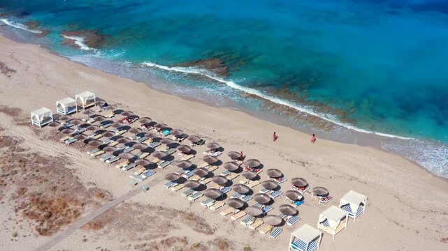 Beach lined with thatch parasols and straw umbrellas on greek island in Greece. Sandy beach and ocean beautiful sea. Aerial view Sunny day summer vacation feeling. huts or tents with sunbeds