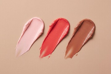 Fototapeta premium Three creamy lipstick swatches in pink red and brown shades smeared on a neutral beige background