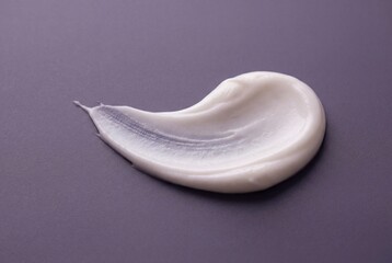 White cosmetic cream smear with smooth texture isolated on a dark purple surface
