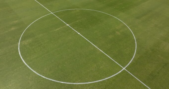 Aerial close-up view of a football pitch's center circle, showing the crisp white circular marking and the halfway line on a well-maintained green grass surface. View from above of soccer ground.