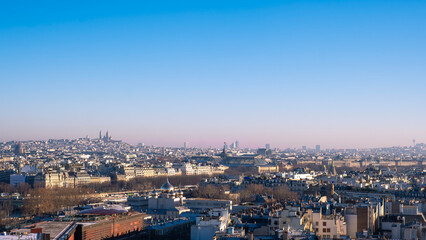Naklejka premium Panoramic view of Paris skyline featuring the Sacre-Coeur Basilica on Montmartre hill. Dense urban landscape with classic architecture under a clear blue sky on a bright day in France