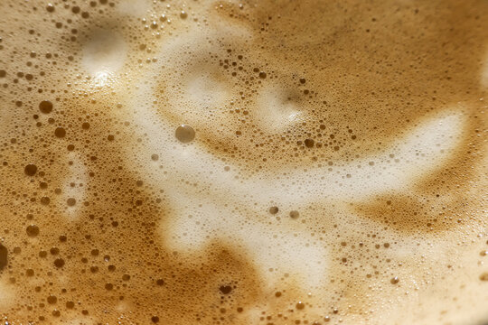 Happy coffee foam latte art in cappuccino beverage. close up brown morning drink with smiling face pattern. An abstract, frothy texture, pleasant cheerful surprise