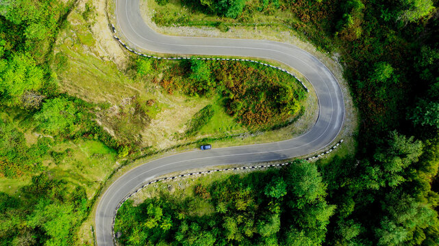 Aerial view with vehicle driving on highway road in green forest. Sustainable transportation, zero emissions, and eco-friendly