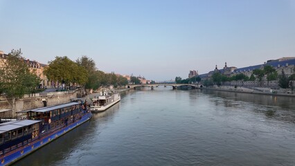 Seine river flowing through paris city center overlooking the pont royal bridge, historic louvre museum and riverboats docked along the quai at dusk © DawDunia