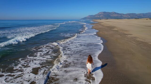 Aerial perspective of woman joyfully running along scenic beach shoreline, travel Patara Antalya Turkey, concept freedom life style.