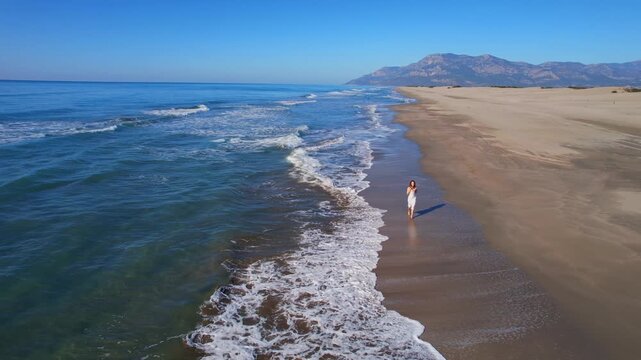 Aerial perspective of freedom woman joyfully running along scenic beach shoreline, travel Patara Antalya Turkey.