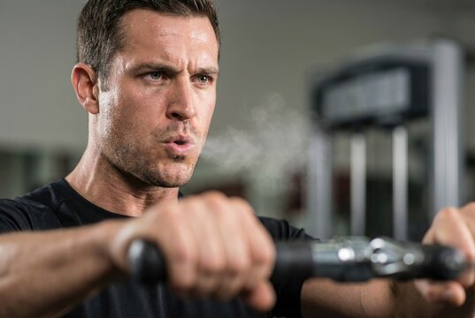 Close-up of a focused athlete breathing out with visible vapor during an intense workout on a machine.