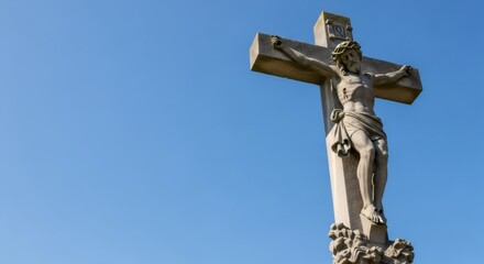 Stone sculpture of Jesus Christ on the cross against a clear blue sky. Christian crucifixion symbolism for Good Friday and Easter.