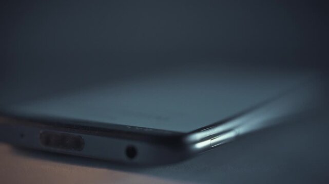 In the dark night, a smartphone screen suddenly illuminates, emitting a radiant glow and shattering the silence with an incoming call or notification on the mobile device