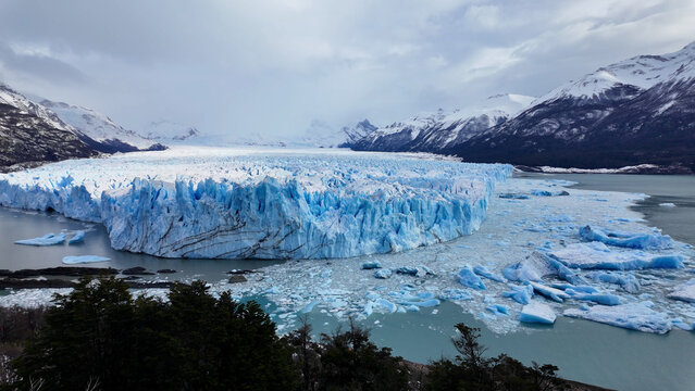 Perito Moreno Glacial In El Calafate Santa Cruz Argentina. Aerial View Of Massive Glacier Calves Into A Lagoon Of Icy Water. Nature Tourism Icon Snow Covered Forest Trees.