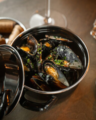Steamed mussels cooked with herbs and garlic served in metal pot on rustic restaurant table