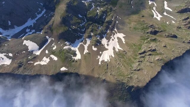 Aerial view of moist air condensing along a high altitude mountain ridge slope in the United States. Orographic cloud formation spreads across rugged alpine terrain under dynamic mountain weather.