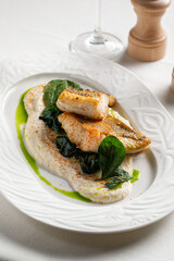 Pan seared white fish served with creamy sauce spinach and herb oil on elegant white plate
