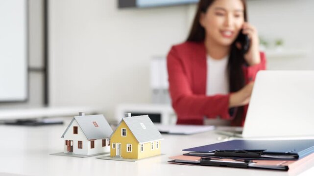 Confident asian business lady, broker real estate agent or manager, sitting at table in a modern office, working with laptop, talking to client or employees on smartphone, smiling.