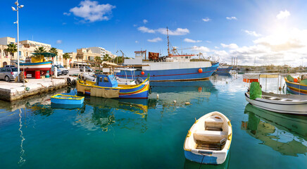 Sunny fishing harbour with small colourful boats, calm water and Mediterranean architecture in Marsaxlokk, Malta