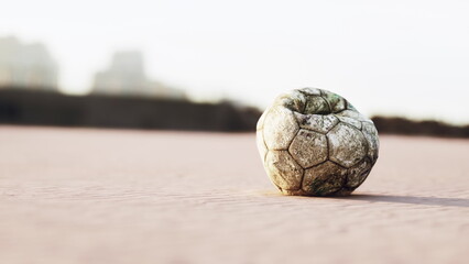 An old, weathered soccer ball rests on a sandy beach, surrounded by soft grains. The sun casts a warm glow, highlighting its worn out texture and faded colors, creating a nostalgic atmosphere.