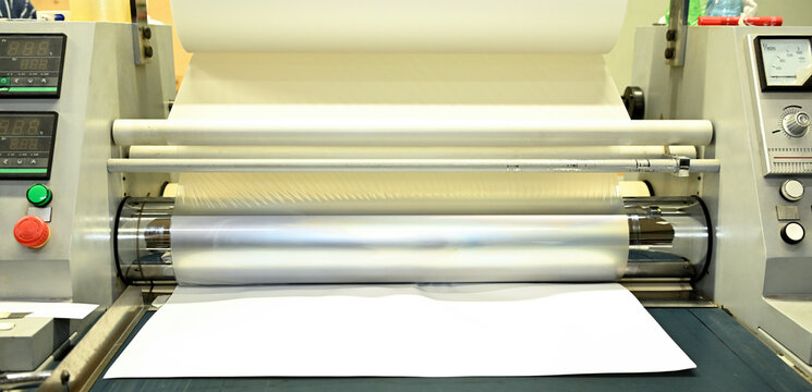 Work behind the laminator in the production shop of the printing house. Industrial laminator for film application.