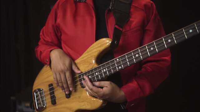 Close-up of bassist playing electric bass guitar in music studio