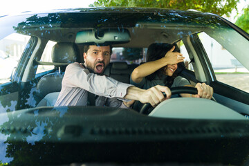 Adult driving instructor reacting nervously to a reckless young female driver during her driving lesson, experiencing fear and danger