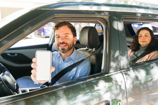 Rideshare driver holding smartphone with blank screen for app mock-up while passenger waits in back seat
