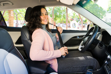 Young Latin woman fastening her seatbelt inside a vehicle, preparing to drive safely and highlighting road safety awareness