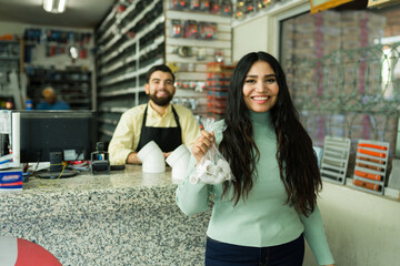 Latin young woman shopping for plumbing supplies at a small hardware store, smiling worker assisting customer