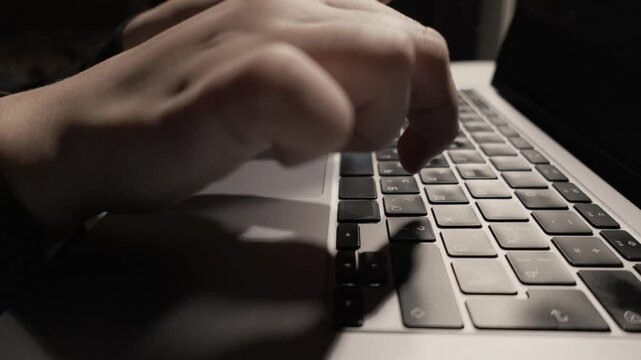 Close-up of hands typing on a laptop keyboard in low light conditions