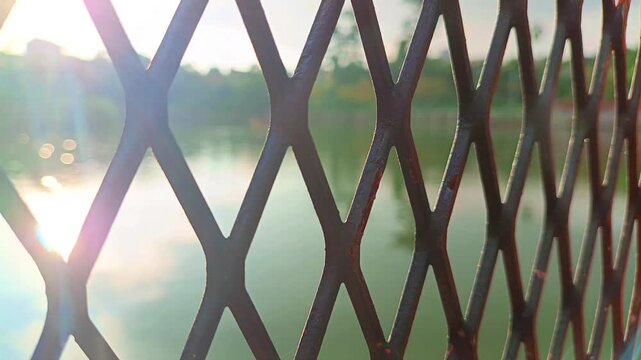 Metal wire fence pattern with river water and soft sunlight in outdoor environment background. Infrastructure concept