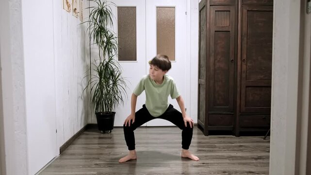 Caucasian boy doing sumo squats lifting heels alternately. Child does sport exercise at home. Children workout. Morning warmup. Strengthening the legs muscles. Strong body. High quality 4k footage.