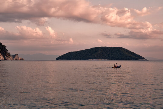 Uomo in canoa al tramonto con isola e scogliere sullo sfondo a Skopelos