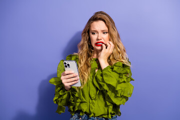 Charming young female model posing with phone in green ruffled shirt against violet background