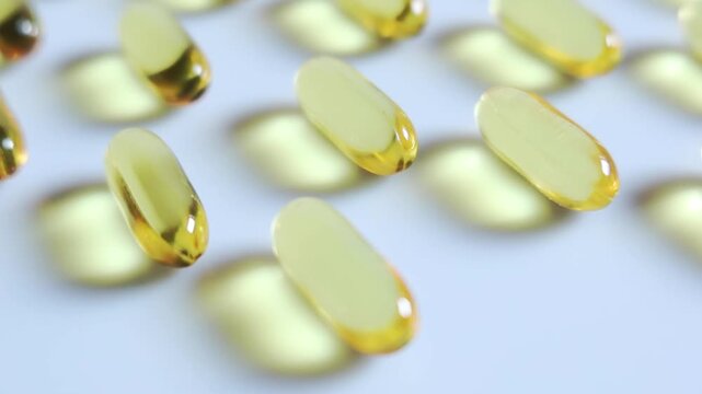 Close up Yellow fish oil capsules on the white floor. Slow motion video.