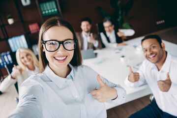 Smiling team of coworkers showing thumbs up during an office meeting, reflecting positivity and...