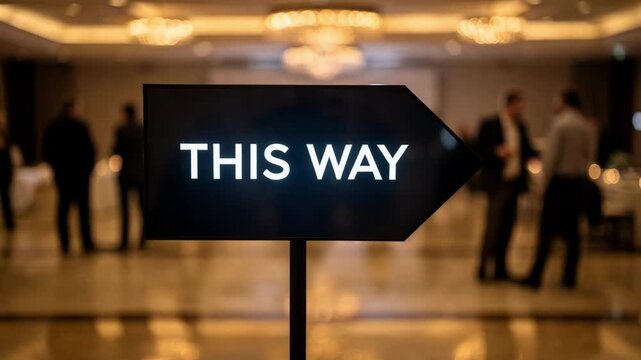 Focused medium shot capturing an illuminated digital arrow sign directing attendees surrounded by outoffocus venue ambiance to highlight navigation clarity.