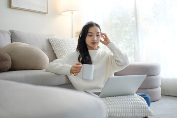 Young woman relaxing on the living room floor while using a laptop and holding headphones, enjoying online content at home.