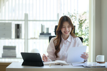 Smiling young businesswoman reviewing documents at her office desk.