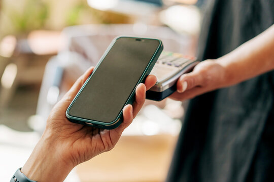 Close-up of a mobile phone touching a card reader in a cafe to make a payment.