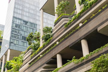 A building with multiple levels shows green terraces filled with various plants. This structure stands in a busy urban area surrounded by glass buildings © Creative_Bird