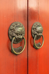 Two bronze lion face knockers with rings are attached to bright red wooden doors. This scene is common in traditional Asian architecture and invites visitors to knock