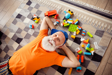 Funny elderly man relaxes on a patterned rug surrounded lego blocks enjoying playful home time...