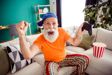Funny grandpa gamer at home cheering with controller bright orange shirt and zigzag pants indoors
