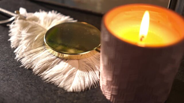 Close-up of a woman's hand picking up a silver bracelet near a burning candle and macrame decoration. Cozy atmosphere for a night routine