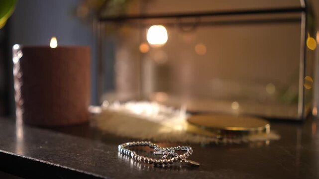 Close-up view of a woman's hand gently placing a silver bead bracelet with a balloon dog charm onto a dark vanity table next to a candle