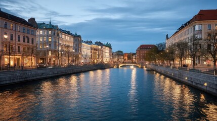 Fototapeta premium Illuminated city buildings along canal at twilight. Urban cityscape with light reflection on water. Travel and tourism concept.