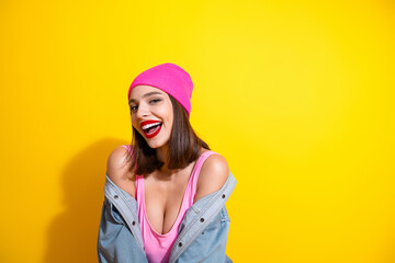 Naklejka premium Young woman in pink beanie laughs in a bright studio against yellow background fashion shoot