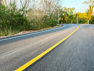 Fototapeta premium an empty asphalt road with a yellow center line leading forward, surrounded by trees and soft sunlight, symbolizing journey, direction, progress, travel, and new beginnings